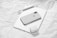 An arrangement of Apple products including a smartphone, tablet, wireless earbuds case, and a stylus on a textured white paper background. The devices are neatly placed, showcasing a sleek and modern design with a minimalist aesthetic.