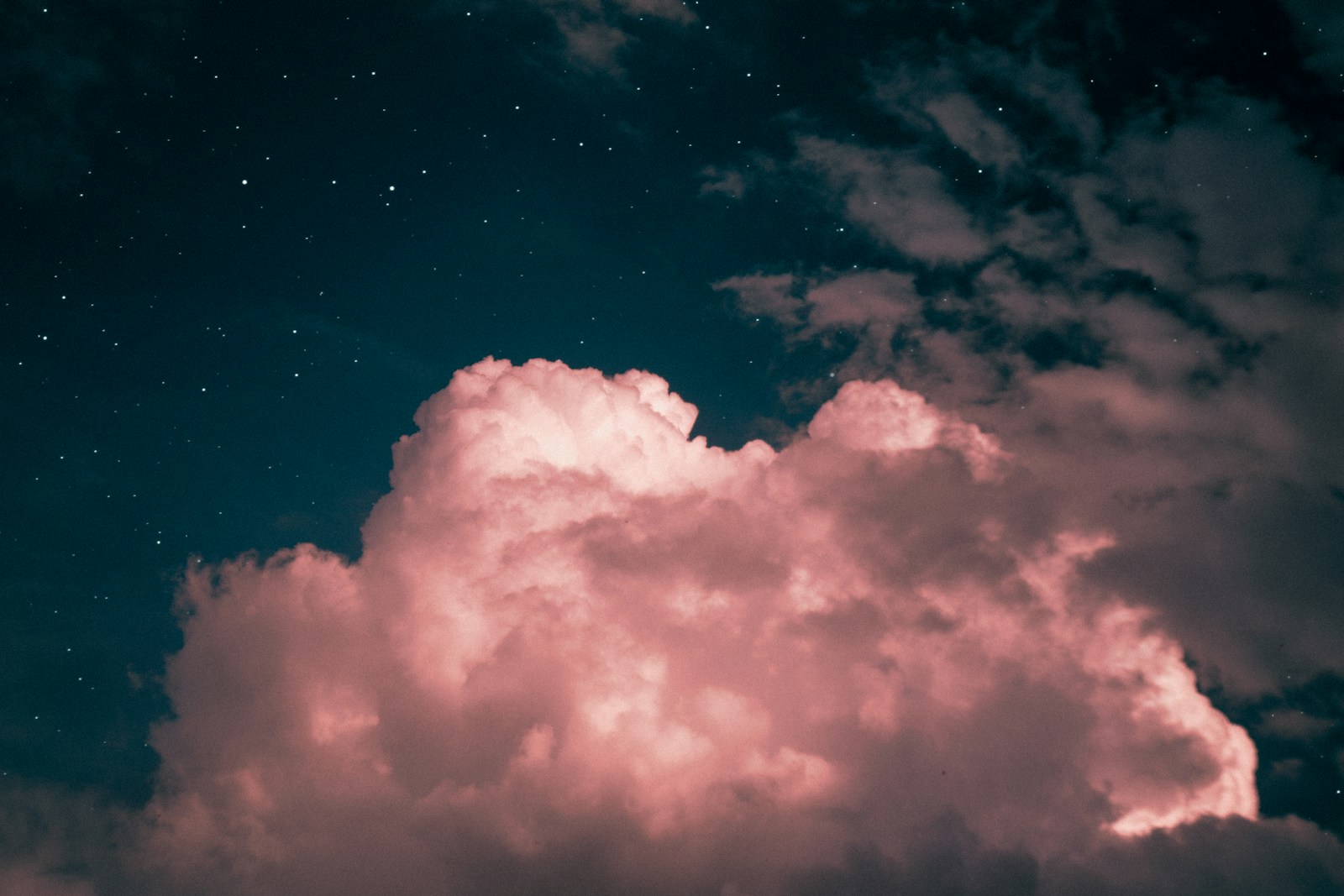 A large cloud lit in pink against a dark star-scattered sky