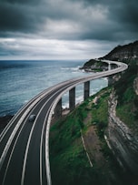gray concrete road bridge near hill and ocean under white and blue sky