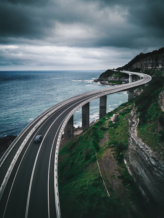 gray concrete road bridge near hill and ocean under white and blue sky in Sea Cliff Bridge Australia