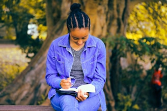 selective focus photography of woman reading book while sitting at bench