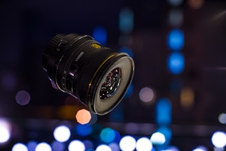 A sleek camera lens focusing sharply against a blurred newsroom background.
