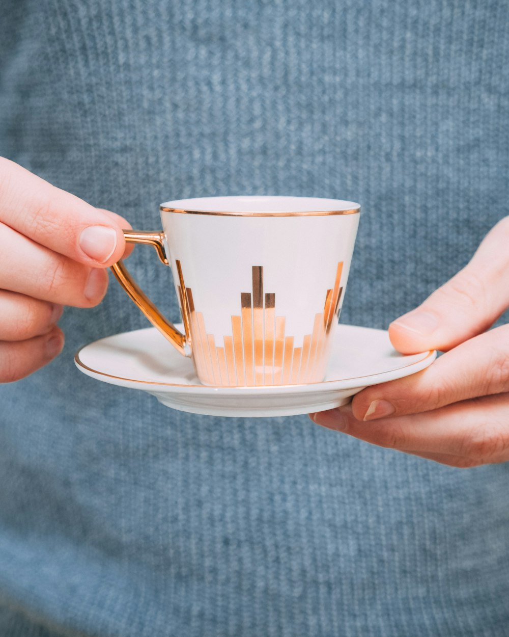 Person mit weiß-goldener Keramik-Teetasse mit Untertasse