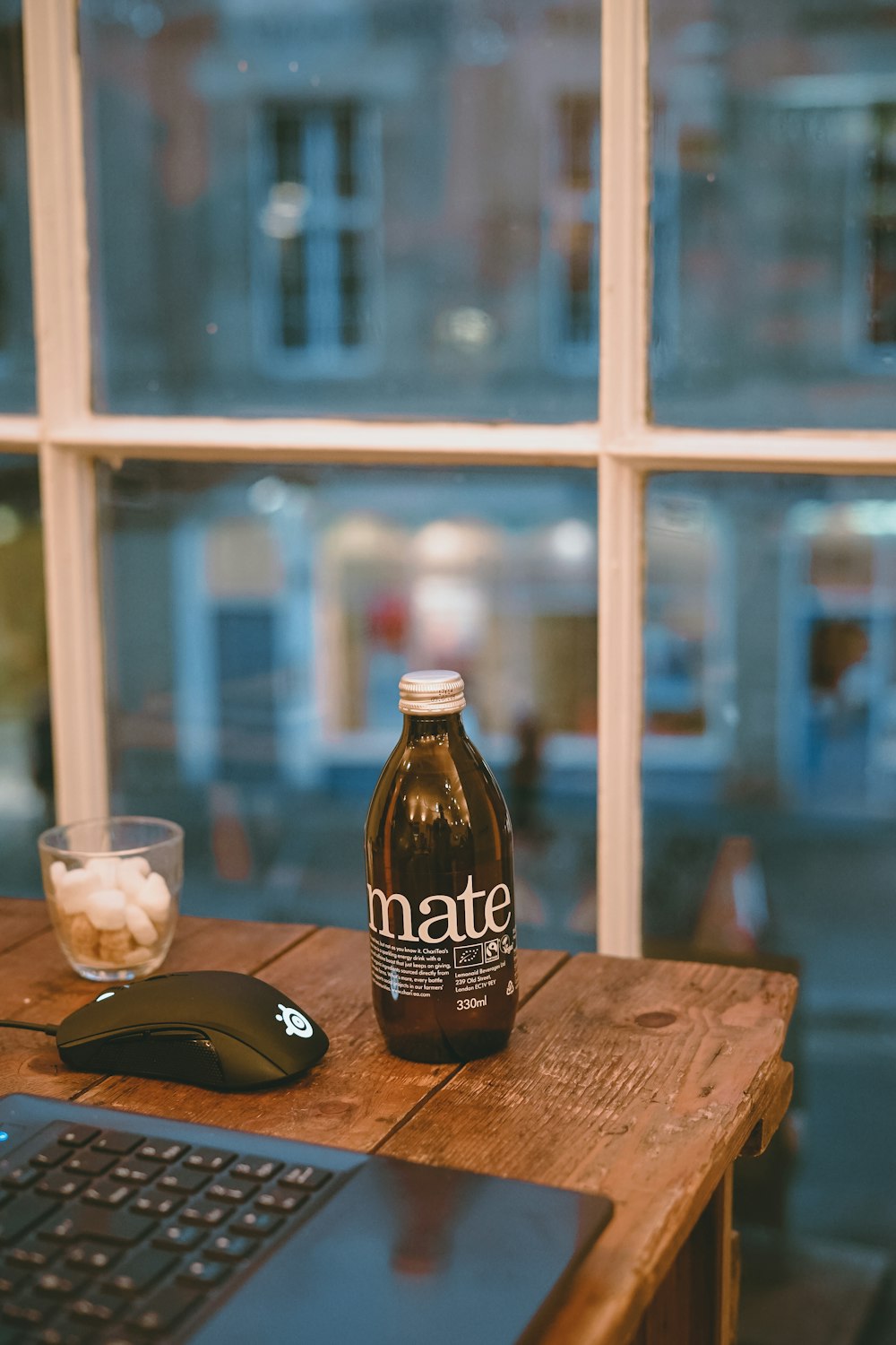 Braune Glasflasche neben Trinkglas und Laptop auf braunem Holztisch