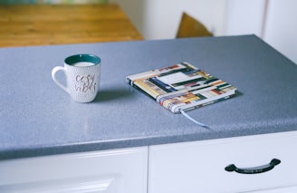 gray and white ceramic mug beside multicolored covered book