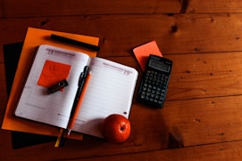 black scientific calculator, orange, and notebook on table