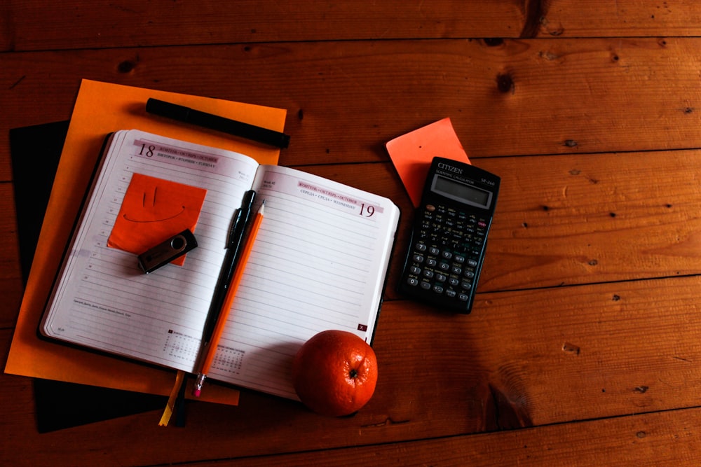 Schwarzer wissenschaftlicher Taschenrechner, orange und Notizbuch auf dem Tisch