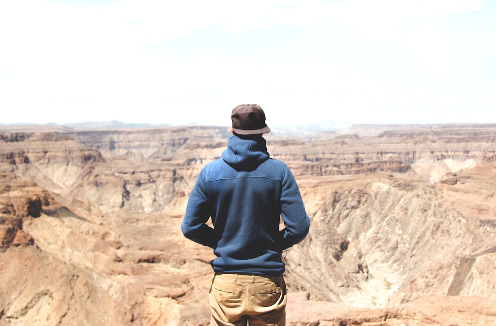 man standing on mountain cliff under cloudy sky