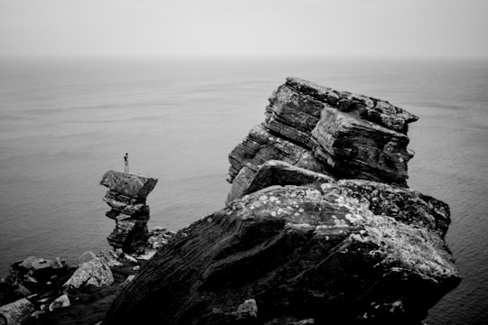 grayscale photography of a person standing on cliff near the ocean in Cliffs of Moher Ireland