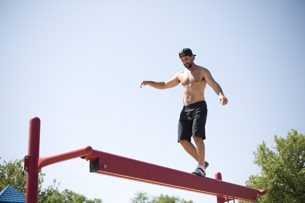 man wearing black shorts walking on red metal beam