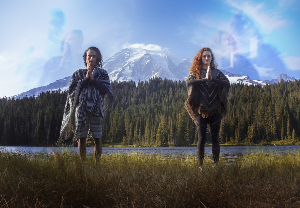 man and woman standing on green grass with snow-capped mountain at distance