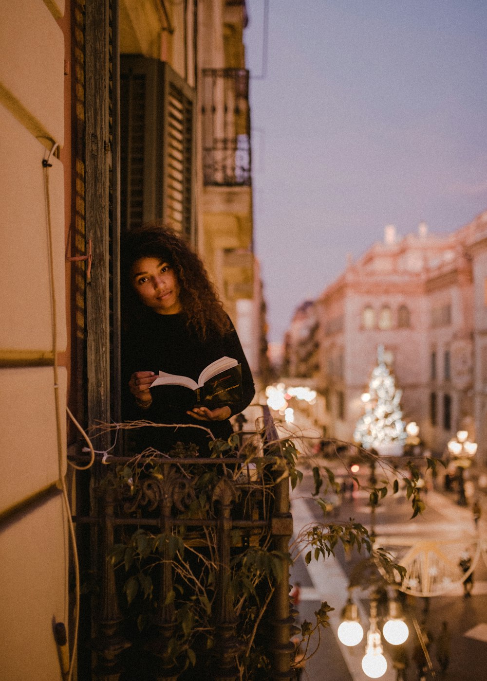 woman holding book standing on terrace during daytime