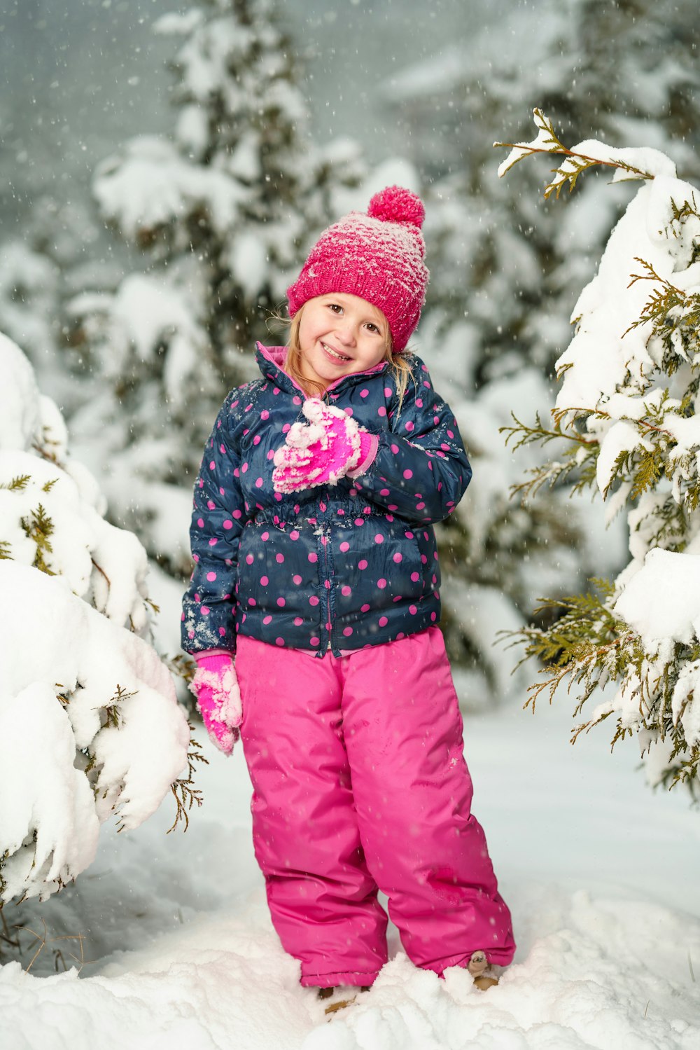 menina em pé na neve branca enquanto sorri perto de árvores cobertas de neve
