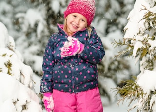 girl standing on white snow while smiling near trees covered with snow