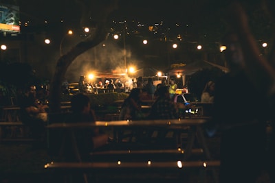A lively outdoor event with guests enjoying a catered meal under warm yellow lighting.