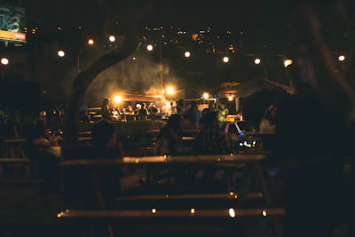 A lively outdoor community gathering with smiling people enjoying music and food under string lights.