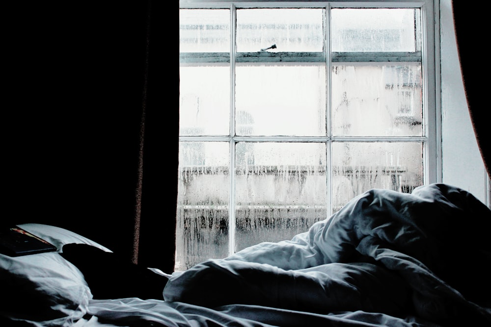 Edredón de cama negro y gris cerca de la ventana de vidrio transparente