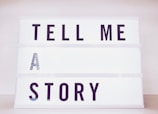 A lightbox with bold black letters spelling out the phrase 'TELL ME A STORY' in an orderly manner with each word on a separate line.