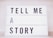 A lightbox with bold black letters spelling out the phrase 'TELL ME A STORY' in an orderly manner with each word on a separate line.