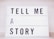 A lightbox with bold black letters spelling out the phrase 'TELL ME A STORY' in an orderly manner with each word on a separate line.