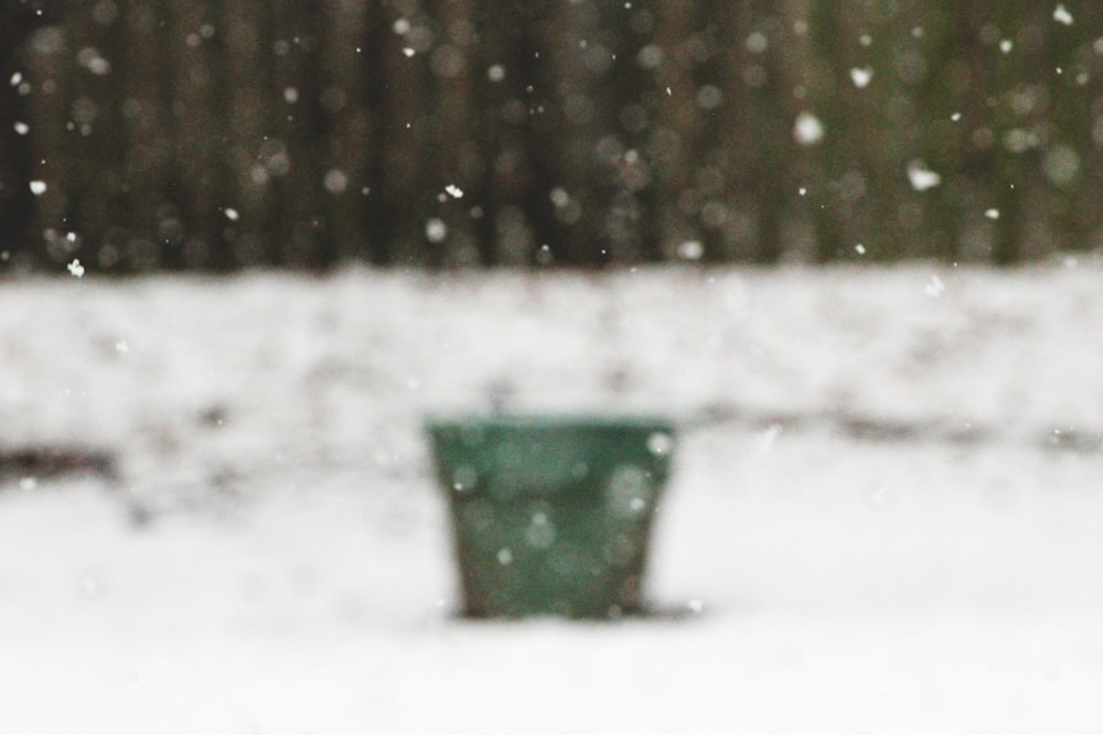 um balde verde sentado em cima de um chão coberto de neve