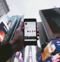 high angle photo of person holding turned on smartphone with tall buildings background