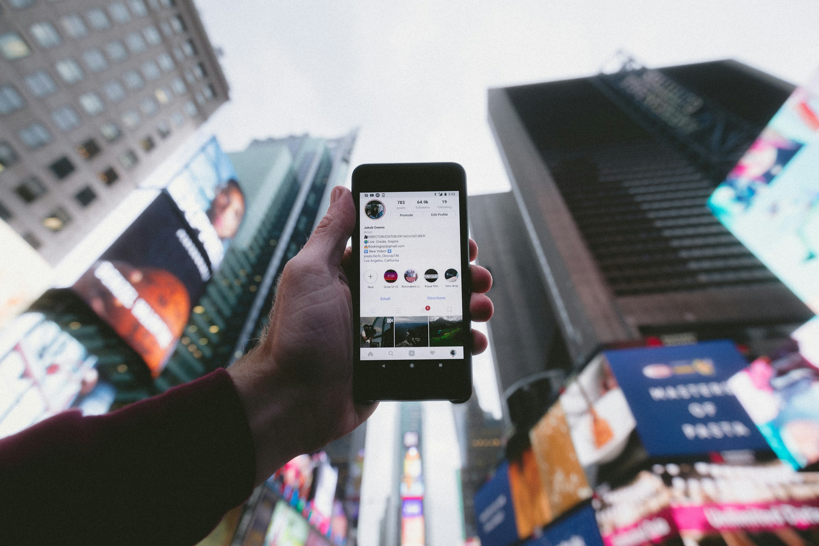 High angle photo of person holding smartphone with tall buildings background