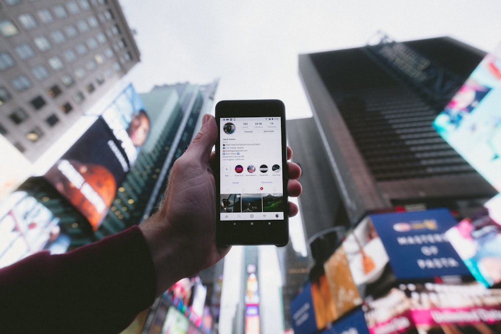 Photo en plongée d’une personne tenant allumé un smartphone avec un fond de grands bâtiments