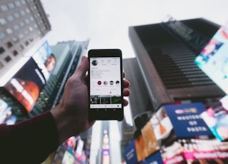 high angle photo of person holding turned on smartphone with tall buildings background