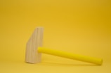 Close-up of a bright yellow and black hammer resting on a wooden surface.