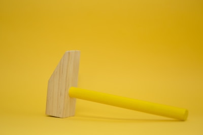 Close-up of a bright yellow and black hammer resting on a wooden surface.