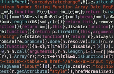 A close-up view of computer programming code written in a variety of colors, including white, blue, orange, and green. The text appears to be JavaScript, featuring syntax elements like functions, variables, and keywords.