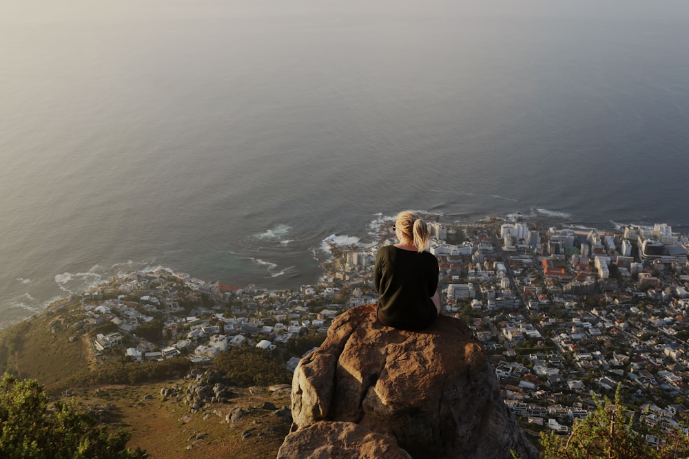 Mujer sentada en la cima de la montaña rocosa que observa la vista de la ciudad