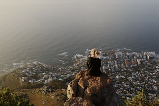 woman sitting on top of rocky mountain watching view of city in Lion's Head South Africa