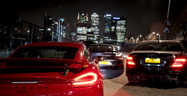 A Porsche parked against a backdrop of towering skyscrapers at night, illuminated by cool blue tones.