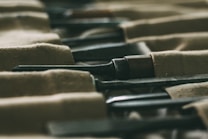 A close-up view of a set of chisels neatly arranged in a fabric holder. The focus is on the metal blades, which are partially covered by the brown cloth. The image is slightly blurred, emphasizing the texture of the fabric and metal.