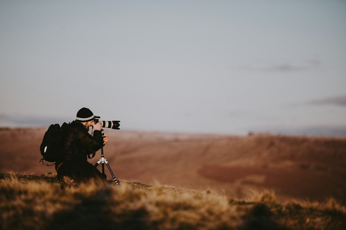 Photographe accroupi dans un champ, appareil muni d'un téléobjectif