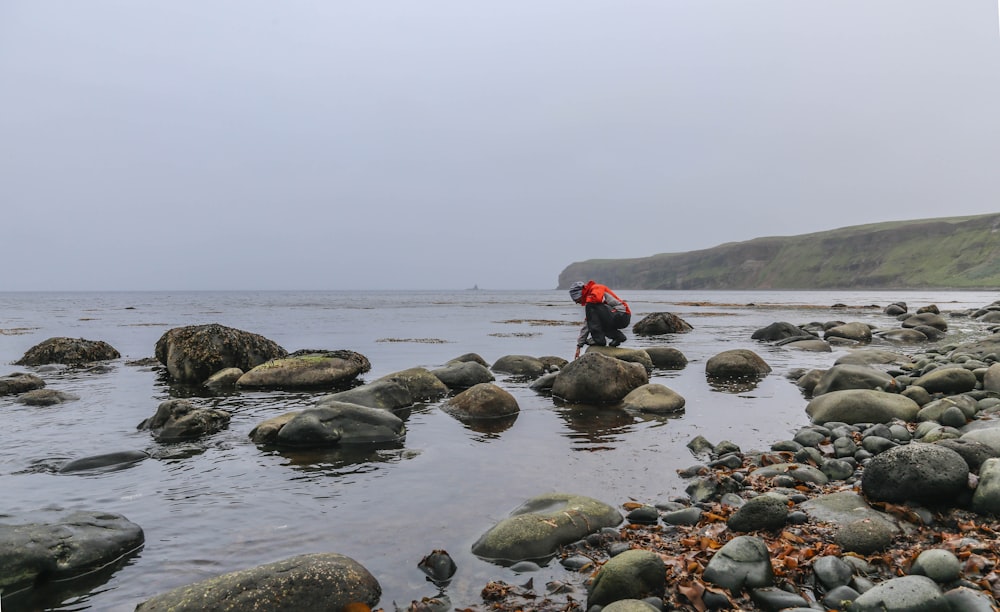 person crouching on rock boulder near body of water