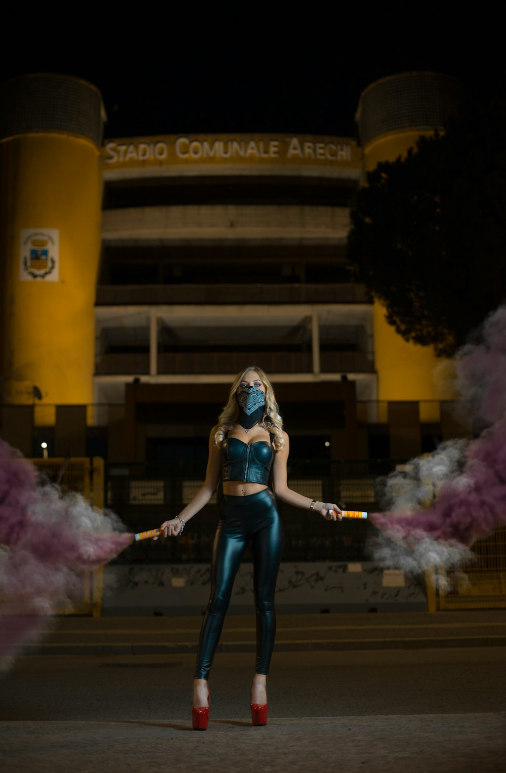 woman standing on pavement holding smoke bombs during night time