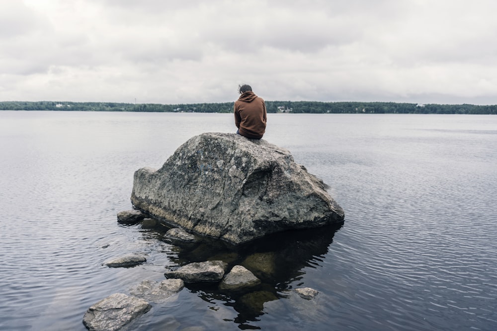 person sitting on rock surrounded by water