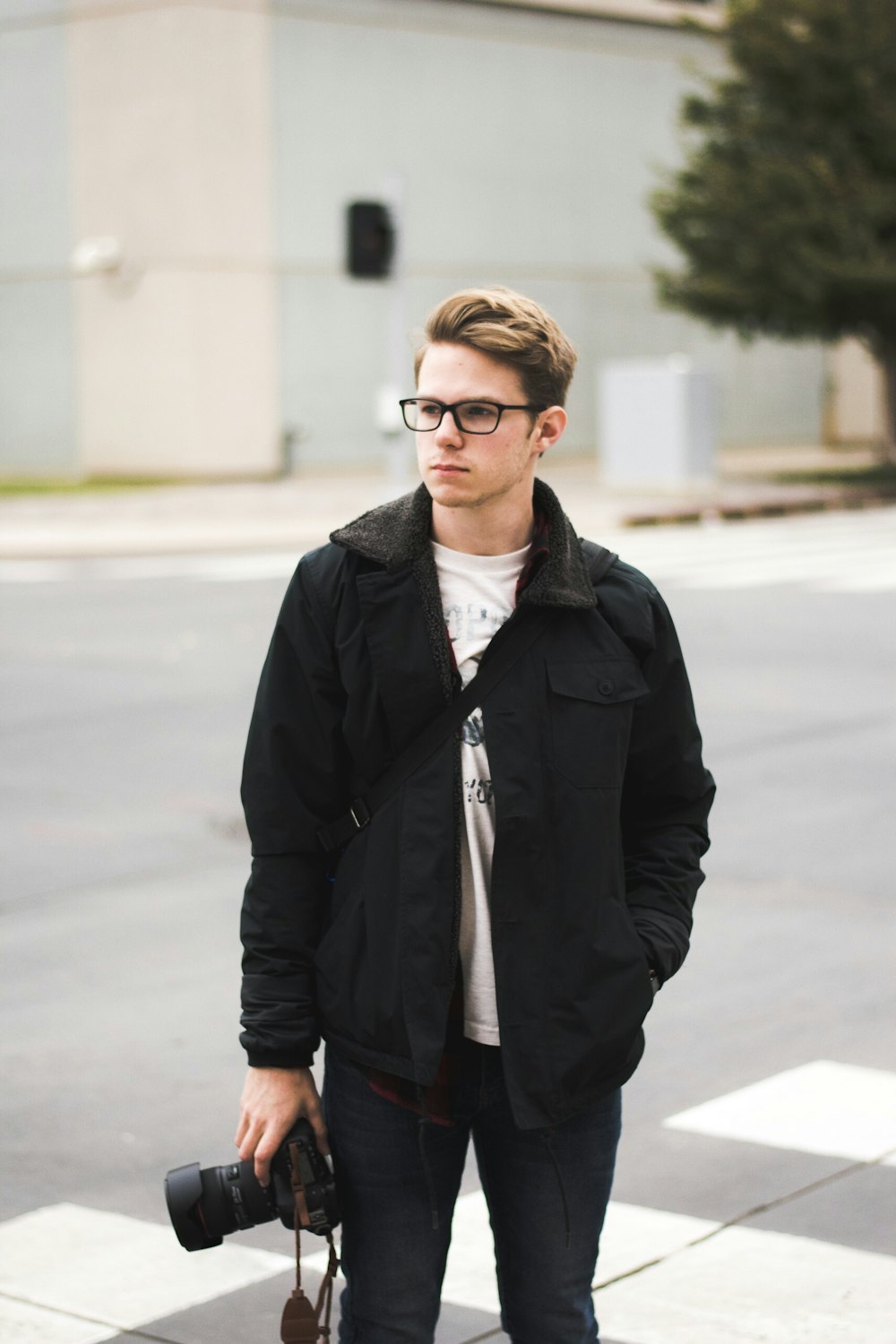 standing man holding DSLR camera wearing eyeglasses and jacket