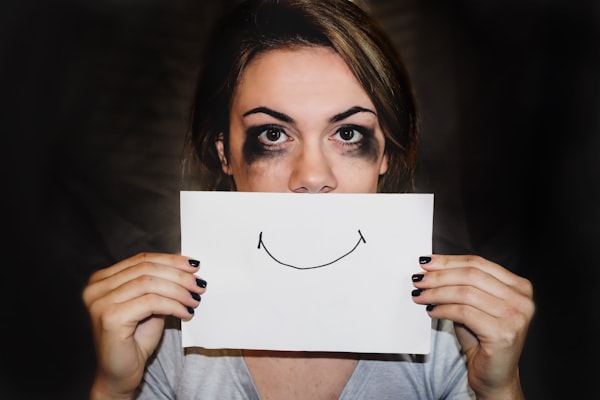 A woman with smeared mascara holding up a picture of a smile over her face.