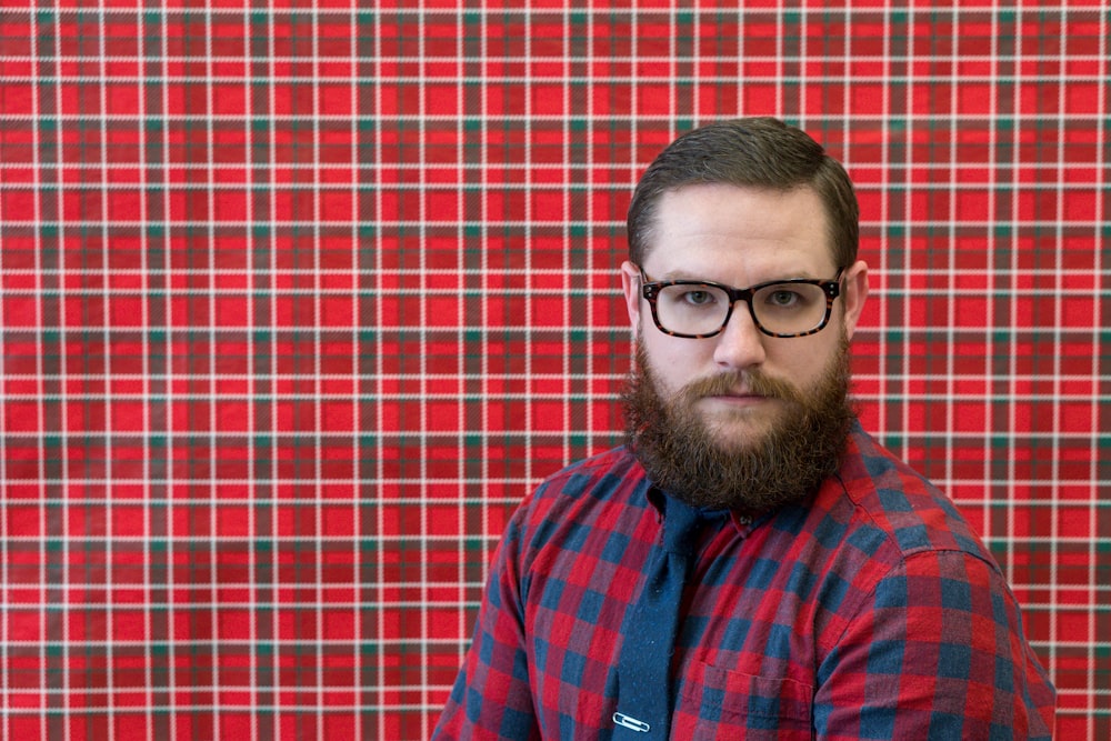 homme portant des lunettes près du mur rouge