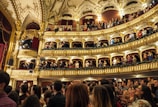 Audience members applauding at a cultural event in a theater.