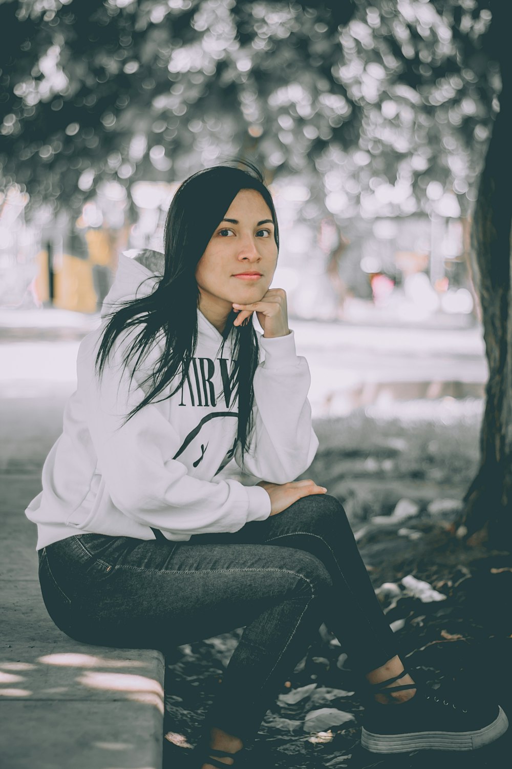 woman sitting on concrete bench with hand on cheek under tree