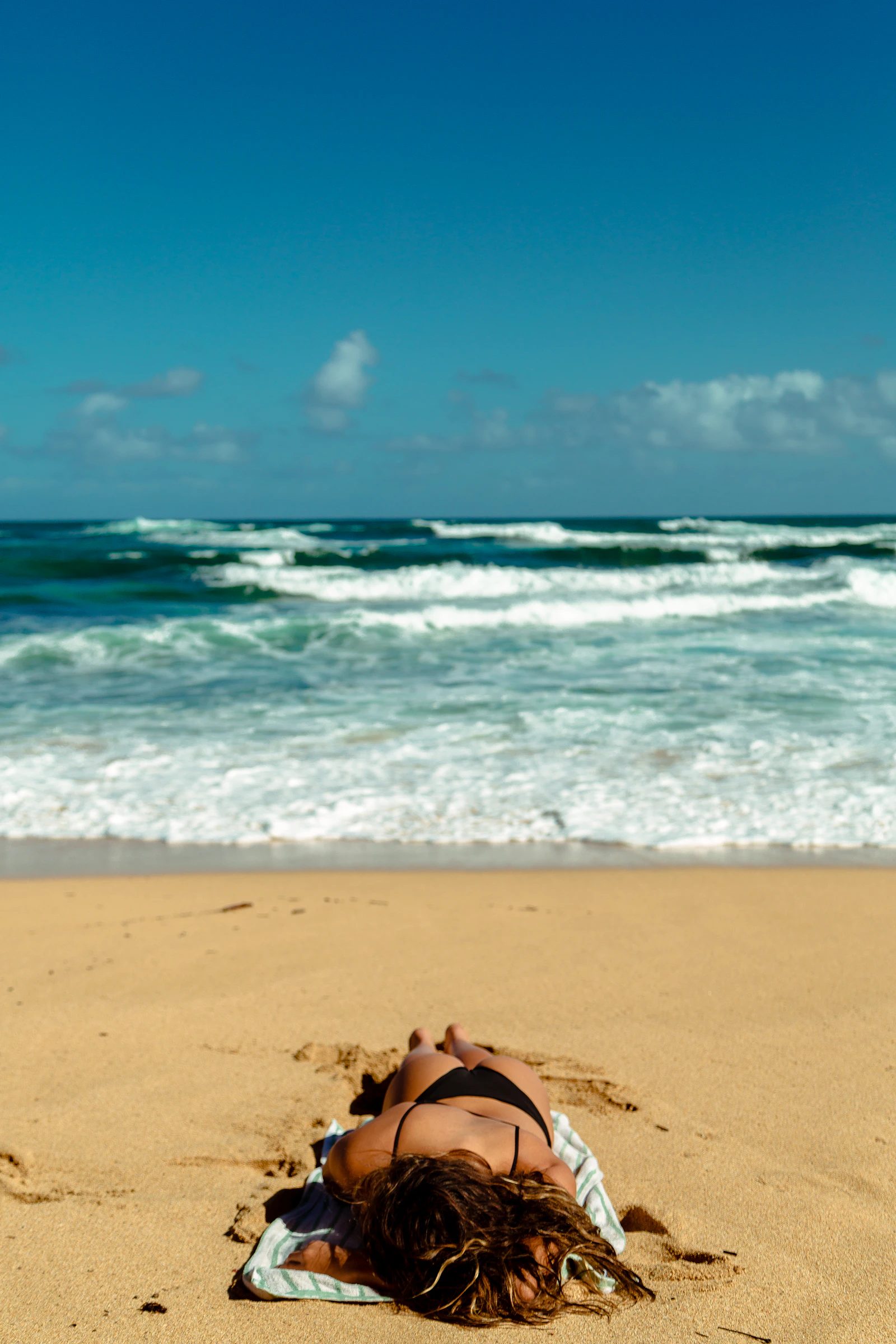 Woman relaxing on a sandy beach near the ocean with belongings on her towel
