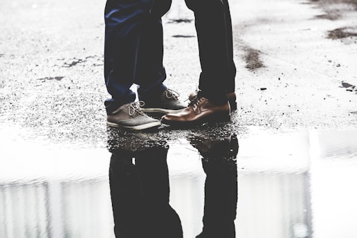 two person standing on road beside body of water