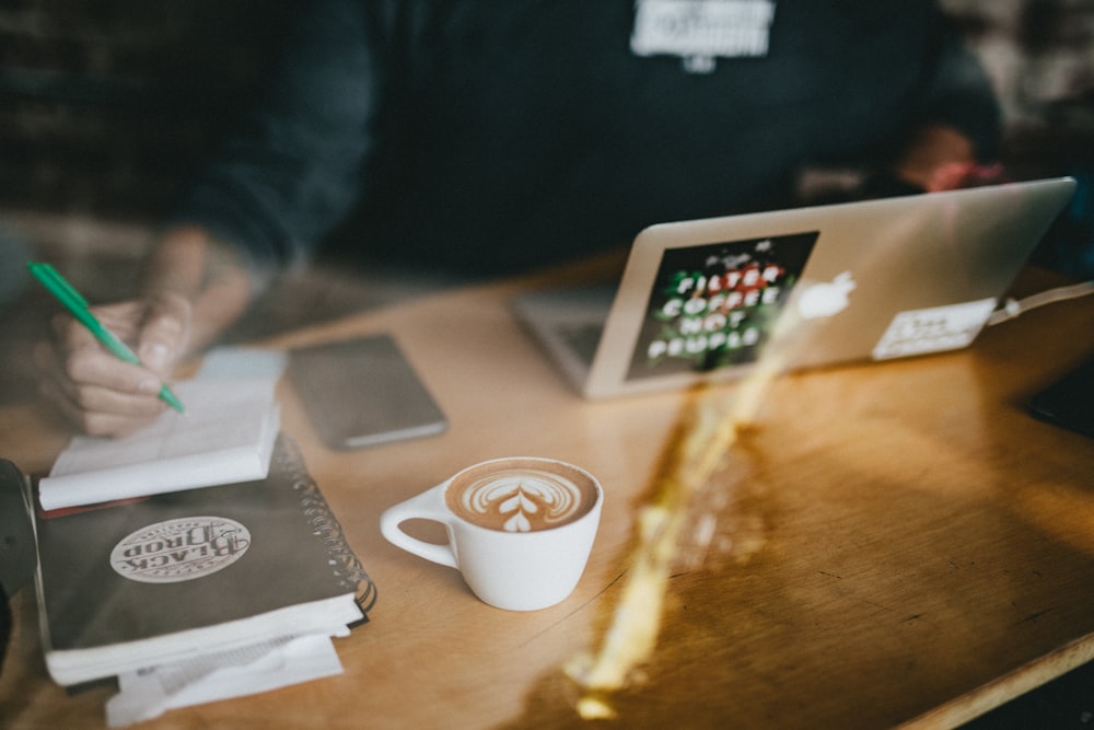 cappuccino art on white ceramic mug beside MacBook Air