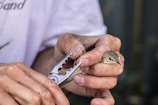 A person carefully holds a small bird in one hand while using a pair of pliers to gently attach a small band to the bird's leg. The process appears delicate and requires precision.