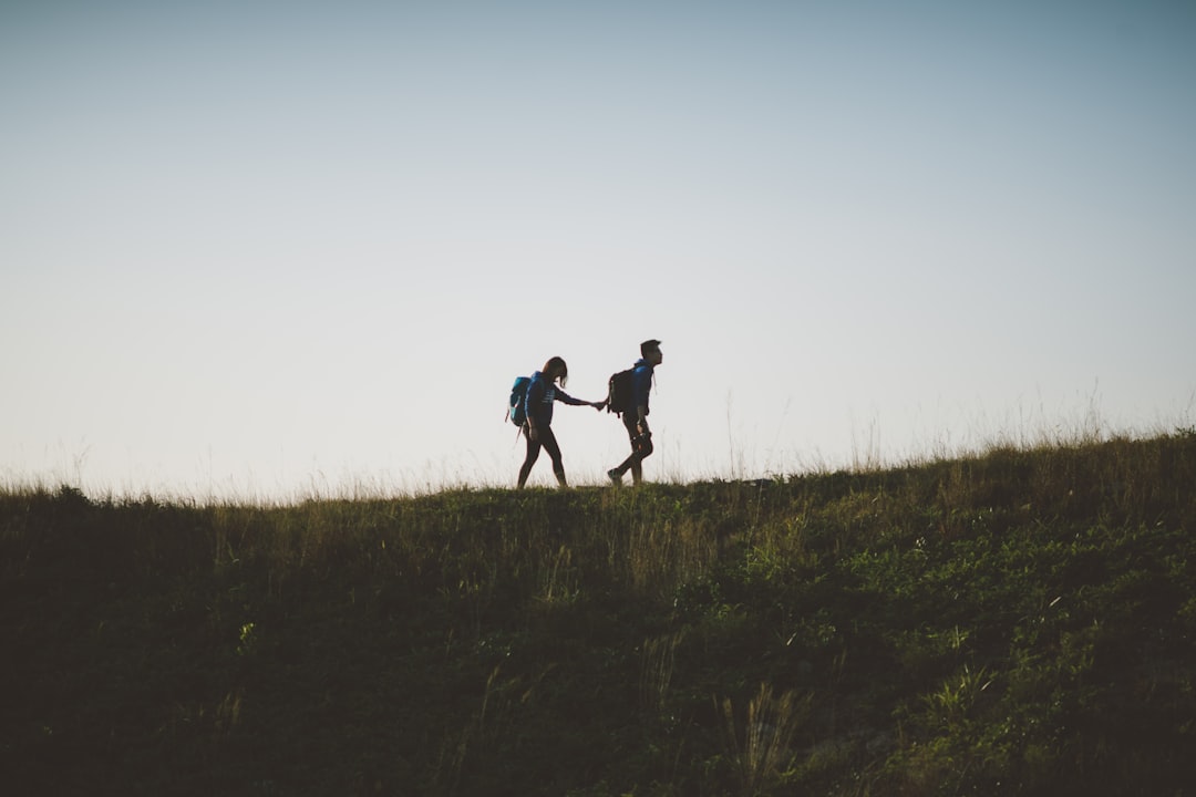 couple walking on hill while holding during daytime, Take my hand